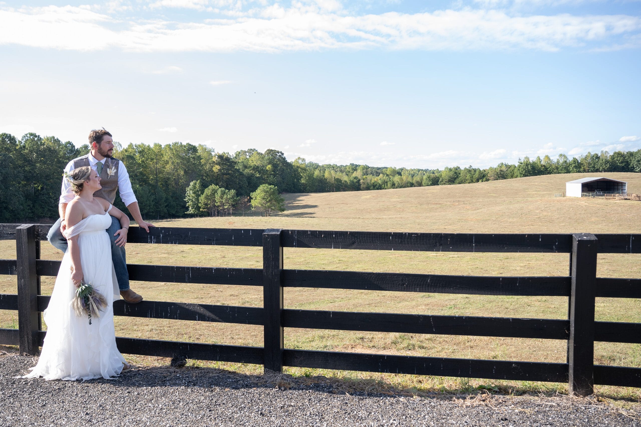 Wedding couple looking away next to the farm wooden fence on a clear sky